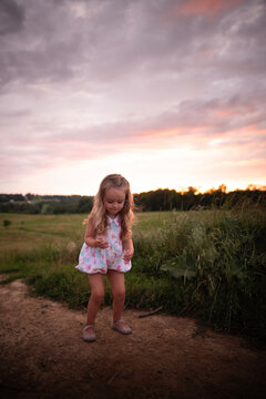 Little girl long blonde curls playing in grassy field colorful sunset
