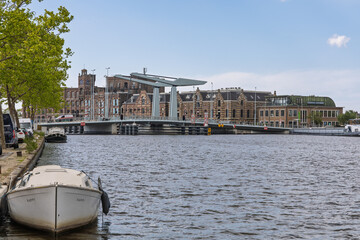 Modern drawbridge over a canal in the Netherlands with historic buildings, boats, and calm water on a clear day in a scenic urban setting. Wormer, Netherlands, 18 May 2025.