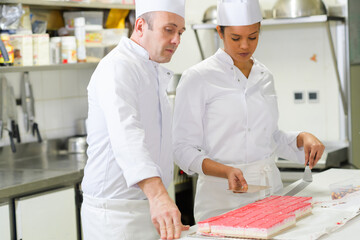pastry chef and apprentice decorate a cake