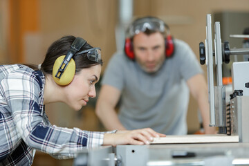 female apprentice using saw in carpentry workshop