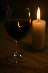 A glass of red wine with a crescent moon glowing through the liquid, next to a flickering candle, creating a serene and intimate ambiance.