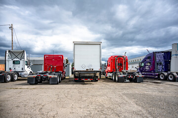 Back view of the different big rig semi trucks and semi trailers standing in row on industrial...