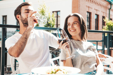 Smiling beautiful woman and her handsome boyfriend. Happy cheerful family. Couple cheering with glasses of red wine at their date in restaurant. They drinking alcohol at veranda cafe in the street