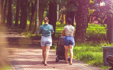 Two girls with a baby stroller are walking in the summer park
