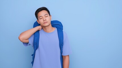 Young Asian man with backpack stretching on blue background, showcasing relaxation amidst travel preparations.