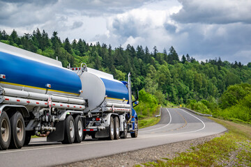 Obraz na płótnie Canvas Day cab blue big rig semi truck tractor transporting fuel in two tank semi trailers running on the winding highway road