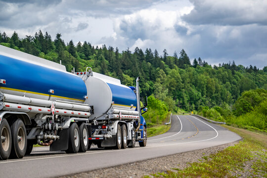 Fototapeta Day cab blue big rig semi truck tractor transporting fuel in two tank semi trailers running on the winding highway road