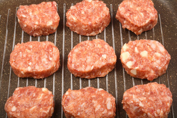 SavoryA close-up, overhead shot shows raw savory minced meat and cheese patties arranged on a dark...