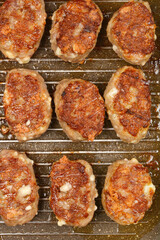 A close-up, overhead shot shows savory minced meat and cheese patties browning on a dark grill pan during cooking
