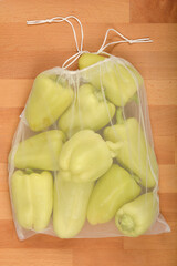 Top-down shot shows a reusable mesh bag filled with fresh, pale green bell peppers, suggesting sustainable grocery shopping