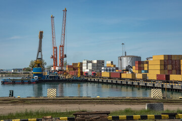 Fototapeta premium Seaport terminal with red cranes, colorful container stacks, port buildings