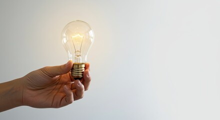 Hands gently holding a light bulb that glows with warm light and minimal background, copyright