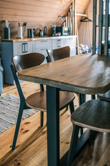 Close-up of wooden dining table and chairs in a modern kitchen with wood-paneled walls, countertop, appliances, and Scandinavian design style