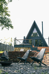 Outdoor seating area with black wooden chairs around fire pit, brick wall background, and modern...