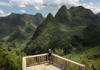 Solo female traveler at the viewpoint overlooking forested hills of Dong Van karst plateau in Ha Giang province in northern Vietnam