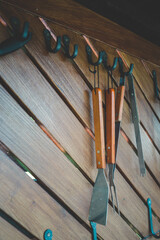 Set of barbecue tools with wooden handles hanging on black metal hooks mounted on diagonal wooden...