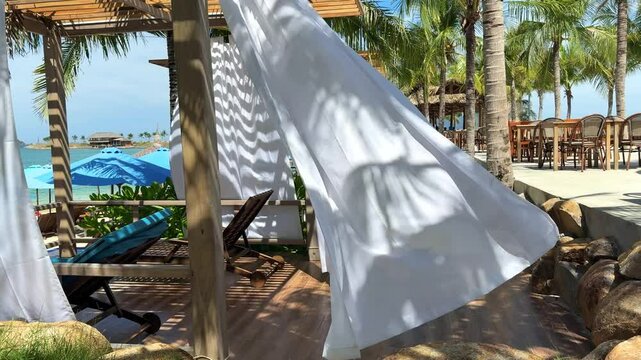 Vietnam, developing white curtains on beach by pavilion. Sun loungers with stoles, wind rippling fabrics, beautiful wedding atmosphere, paradise vacation in the Maldives, palm trees all around