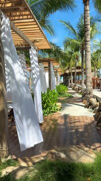 Vietnam, developing white curtains on beach by pavilion. Sun loungers with stoles, wind rippling fabrics, beautiful wedding atmosphere, paradise vacation in the Maldives, palm trees all around