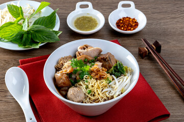 Stewed beef noodles, a Thai street food, and vegetables in a bowl on a wooden table.