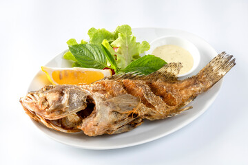 Fried sea bass Fried until golden crisp, in a white dish,  on a table.