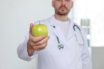 Nutritionist with green apple and stethoscope in clinic, selective focus