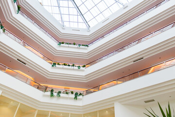Obraz premium Contemporary hotel atrium with several floors, indoor balconies decorated with plants, and warm ambient lighting. A glass roof allows natural light to enhance the elegant architectural lines.