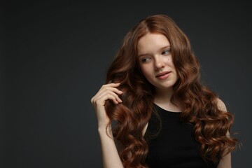 Naklejka premium Portrait of beautiful teenage girl with healthy wavy hair on dark grey background. Space for text