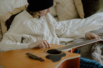 Teenager boy playing acoustic guitar on bed