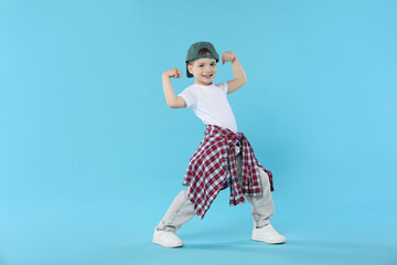 Happy little boy in baseball hat dancing on light blue background