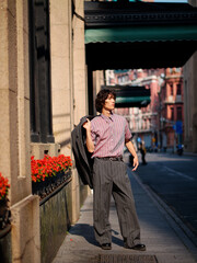 Portrait of handsome Chinese young man wearing gray suit posing in the street, young guy with black curly hair with urban background. Male fashion, cool Asian young man lifestyle.