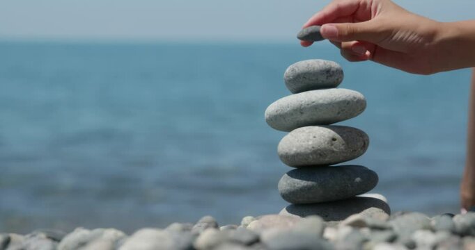 Delicately balancing pebbles by hand on serene ocean beach, creating meditative stone stack representing tranquility and mindful connection with nature's harmony