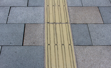 Gray and brown pavement with yellow tactile tiles. Yellow tactile paving on walkway, guiding block for blind and visually impaired.