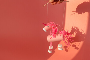 Handmade pink unicorn marionette toy crafted from cardboard tube, yarn, and plastic caps on pink background. Puppet show and childhood creativity concept. Minimal composition with copy space, © Elena