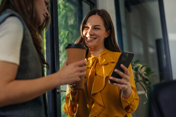 Gen Z businesswomen enjoying coffee break and using smartphone in modern office