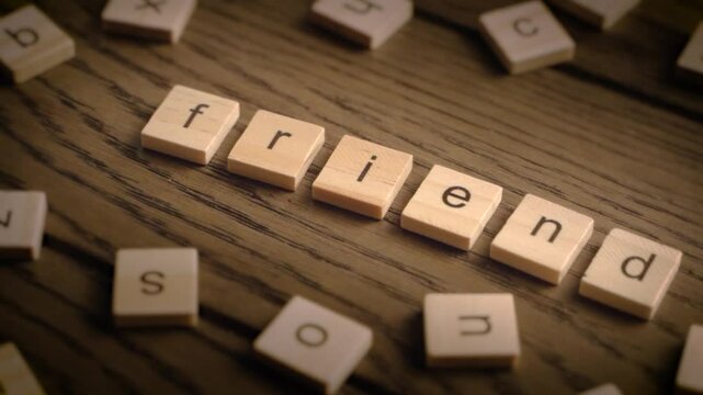 Wooden scrabble tiles spell the word friend as the camera pans across a rustic wooden surface in warm light.