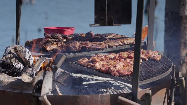 Close up shot of chinchulines and various cuts of meat sizzling on a traditional Argentinian asado. Smoke rises from the hot coals as the barbecue cooks outdoors. A true feast.