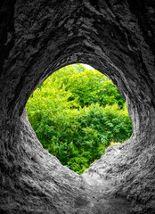 View from a black and white limestone cave into the green countryside with fresh spring foliage. The "Gruermannshohle" cave in famous "Pater und Nonne" rock formation in lserlohnis a natural monument
