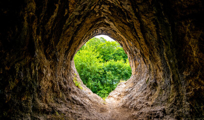 Wide angle view from a limestone cave into the green countryside with fresh foliage. The "Gruermannshohle" cave in the "Pater und Nonne" rock formation in lserlohn. Light at the end of the tunnel.