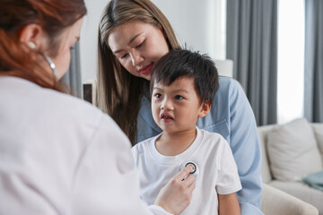Asian Female doctor examining young boy with stethoscope, caring mother holding child, healthcare concept