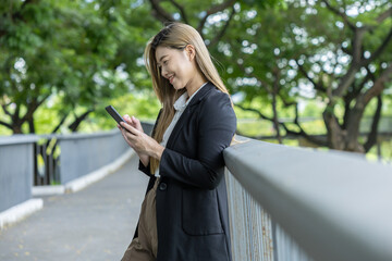 Fototapeta premium Asian Young woman smiling using smartphone outdoors in park