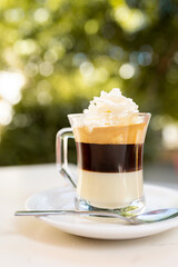 Vertical photo of a glass of coffee with hot chocolate and cream on top on a table in a sidewalk...