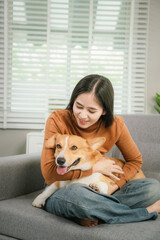 A cheerful young woman sits at home on a comfortable sofa, happily hugging her cute dog in a warm and loving home.