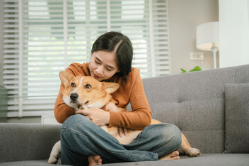 A cheerful young woman sits at home on a comfortable sofa, happily hugging her cute dog in a warm and loving home.