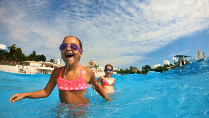 A close-up shot of two young girls in pink swimsuits and goggles splashing in a pool, enjoying...