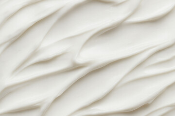 Close up of white whipped cream swirled neatly on top of a rich hot chocolate in a clear glass mug, sprinkled with cocoa powder.