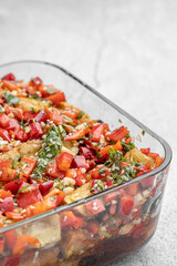 Mediterranean roasted vegetables in a salad bowl on a white rustic table with ingredients.Roasted yellow and red bell pepper salad with capers and olives in a blue bowl on a white background. 