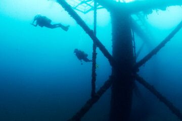 unrecognizable divers diving next to the structure of a sunken wreck in the sea, concept of scuba diving and underwater adventure, copy space for text, copy space for text