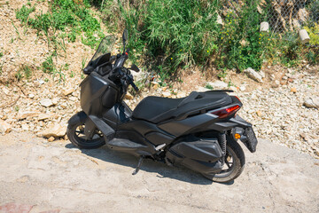 Black modern scooter parked on sunny street. Urban motorbike transportation concept.
