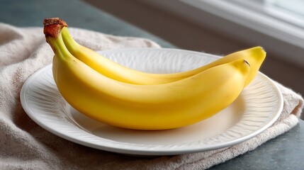 Two ripe bananas placed on a white plate over a cloth napkin near a window