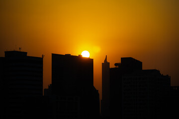stunning silhouette of a city skyline against a vibrant orange sunset. The tall buildings are outlined against the bright sky, creating a dramatic and captivating scene